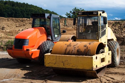 Yellow and orange road rollers parked at a highway construction site