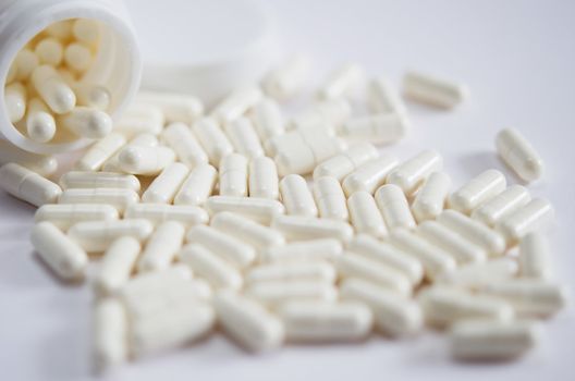 white pills spilling out of  pill bottle on white background