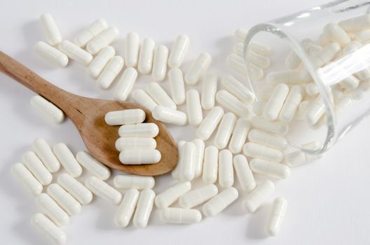 white pills spilling out of glass and pills on spoon