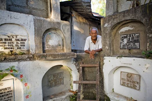 Bacolod City, Philippine Islands, March 2, 2012 - Homeless elderly Filipino man living among stacked concrete tombs in a cemetery.