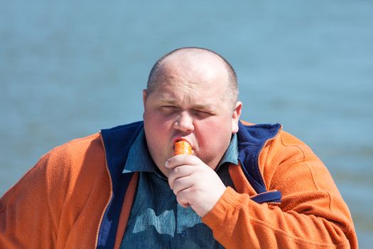 Fat man eating a carrot, on a background of water