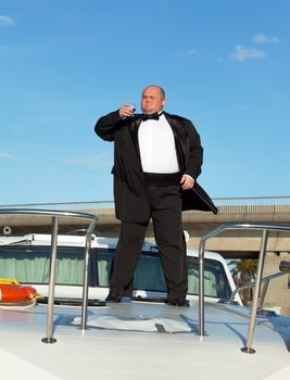 Overweight man in tuxedo standing on the deck of a luxury pleasure boat with glass red wine