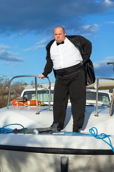 Overweight man in tuxedo standing on the deck of a luxury pleasure boat