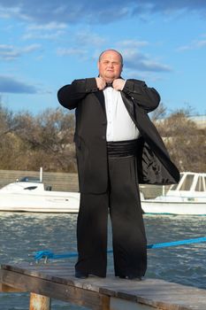 Overweight man in tuxedo standing on the pier marina