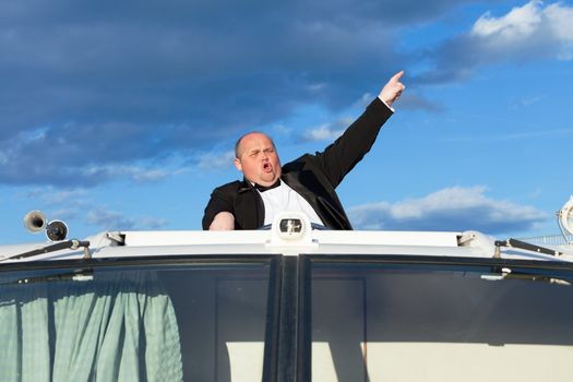 Overweight man in a tuxedo at the helm of a pleasure boat, closeup