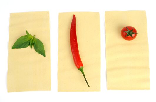 An image of basil, pepper and tomato on raw lasagna 
