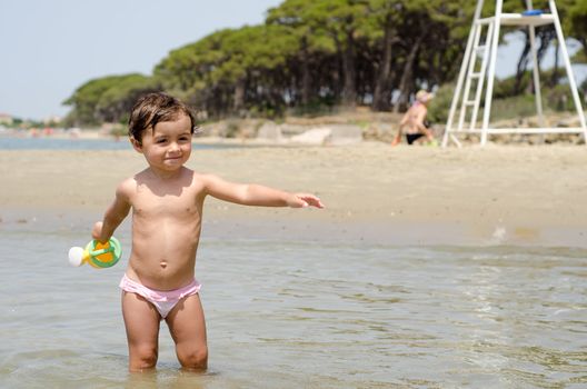 Happy Baby playing with a bucket of water at the beach, Italy