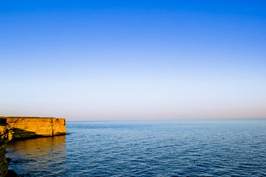 sunset with calm water, blue sky and the rock