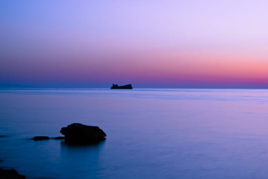 sunset with calm water, blue sky and the rock