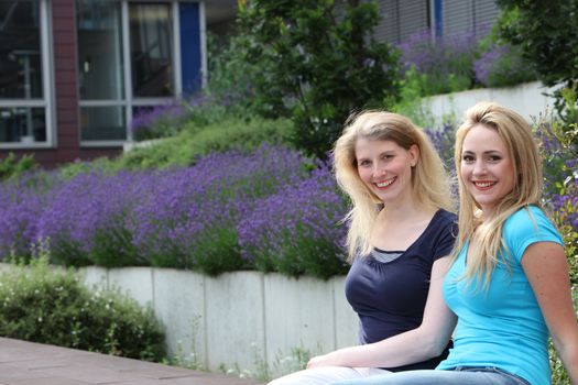 Two colleagues sitting together on a wall outside the office relaxing during lunchbreak Two colleagues sitting together on a wall outside the office relaxing during lunchbreak