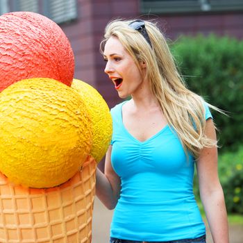 Vivacious blonde woman having fun with an outsized publicity model of an icecream cone as she reacts in open-mouthed awe