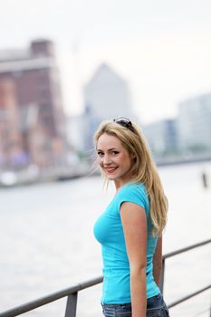 Young smiling female tourist looking back over her shoulder at the camera as she stands alongside an urban river 