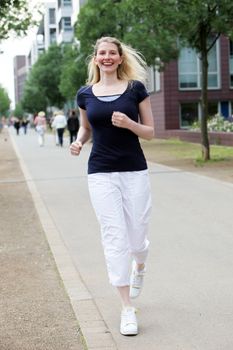 Happy athletic woman jogging along an urban sidewalk as she undertakes her daily exercise routine 