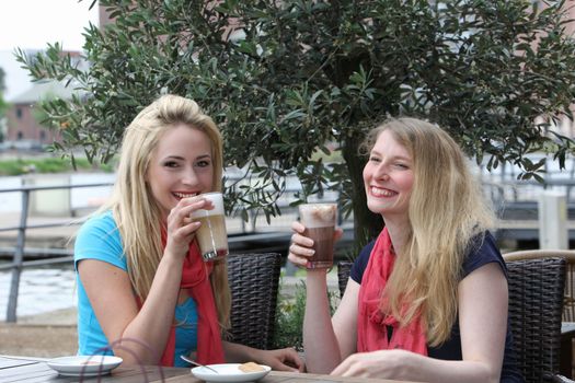 Laughing trendy woman relaxing over drinks seated at a table at an open-air restaurant