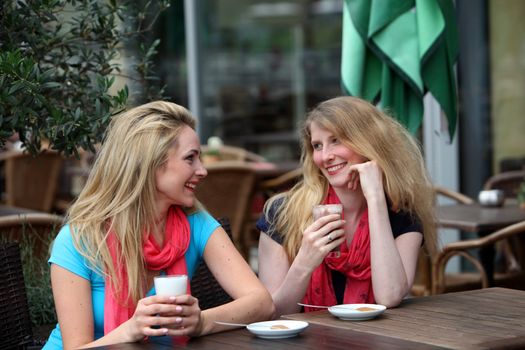 Two ladies seated at a restaurant table chatting together as they sip a glass of iced cool beverage Two ladies seated at a restaurant table chatting together as they sip glasses of iced cool beverages 