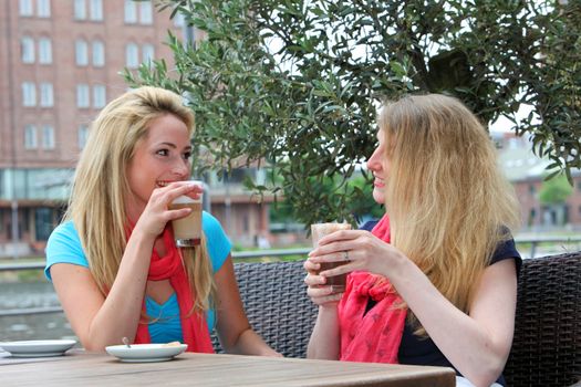 Two elegant female friends sitting at an outdoor cafe chatting over refreshments 