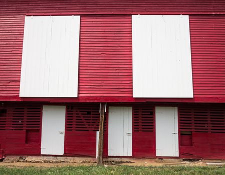 Red painted wooden barn with white door on farm in traditional US style