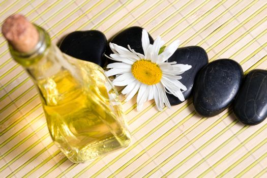 An image of a chamomile, oil  and black stones