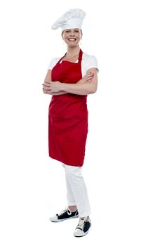 Full length portrait of pretty female cook standing with arms crossed over white