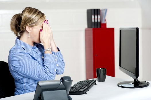 Female secretary hiding her face with hands sitting in front of computer screen