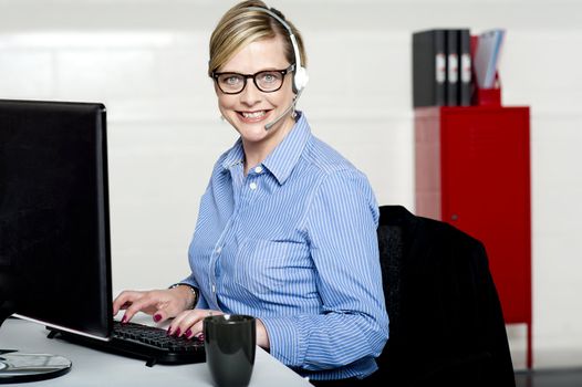 Smiling help desk woman typing on keyboard wearing headsets with mic attached to it