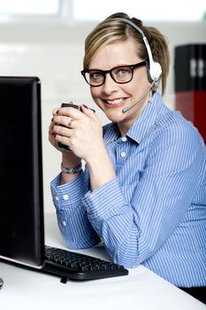 Help desk executive drinking coffee at work and looking at camera