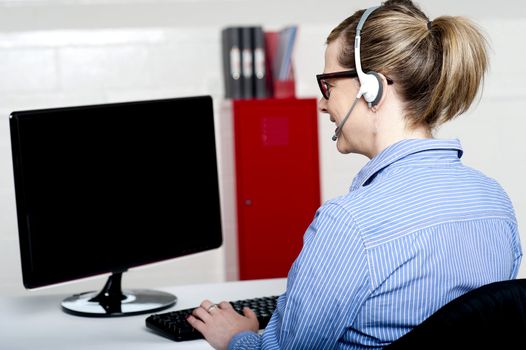 Back view of help desk lady working on computer with headsets on