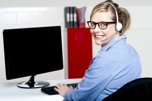 Portrait of cheerful customer support executive looking behind and smiling at camera