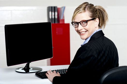 Business lady turning back and smiling at camera while typing on keyboard