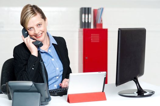 Smiling female secretary attending phone call and looking at camera
