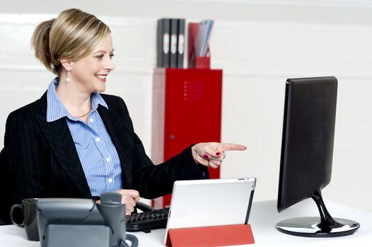 Female executive pointing at computer screen sitting on desk and working