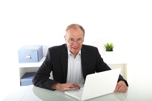Senior businessman working on his laptop seated in his office at his desk 