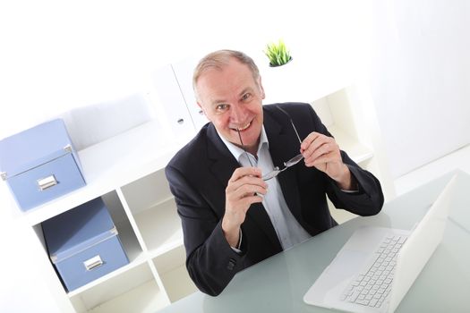 Tilted angle view of a happy middle-aged businessman leaning on his desk with his elbows and smiling at the camera 