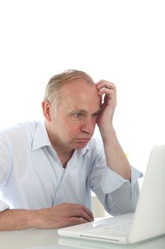 Frustrated bemused man pulling a face as he leans on his desk looking at his laptop Frustrated bemused man pulling a faxce as he leans on his desk looking at his laptop 