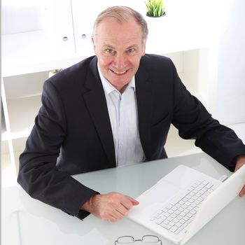 High angle view of a middle-aged enthusiastic business executive seated at his desk in front of his laptop 