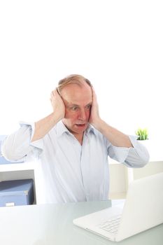 Man seated at a desk reacting in shock with his hands to his face as he reads the screen on his laptop 