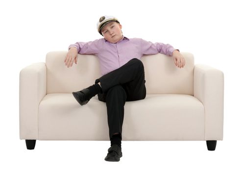 Serious young boy wearing a cap captain sitting on the couch