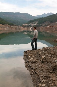 man with a fishing rod on the bank of a mountain lake