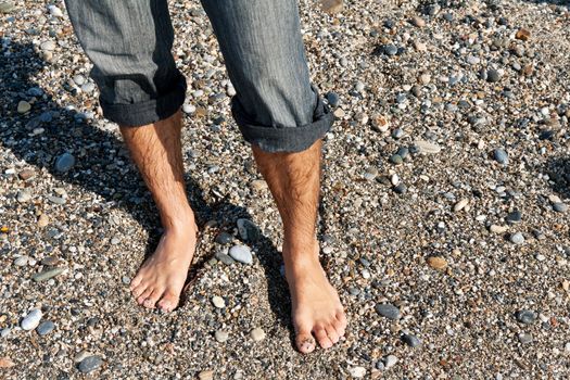 pair of men's feet on the beach with pebbles
