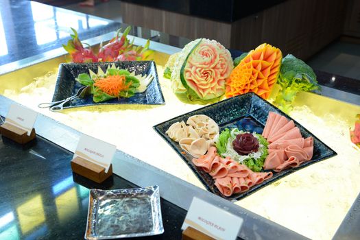 meat delicatessen plate including bologna plain and bologna chilli next to Fruit carvings on the buffet table gson the buffet table