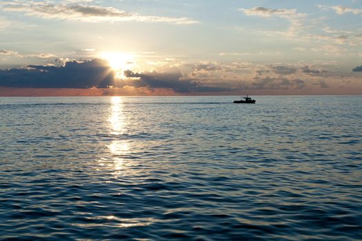 Small boat sailing on the sea at sunset and clouds