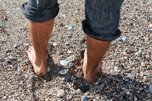 pair of men's feet on the beach with pebbles