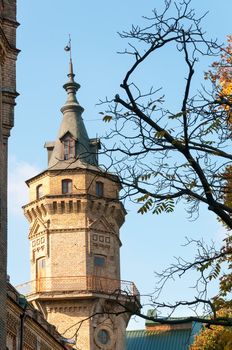 Vintage brick tower with autumnal branches on front and blue sky. Focus on the tower.