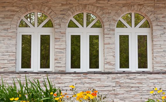 Three windows in the stone wall with a reflection of the forest