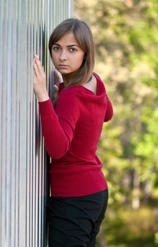 Beautiful girl in purple dress outside steel wall against the background of the forest