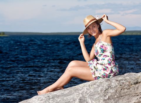 girl in a straw hat sitting on a rock by the lake