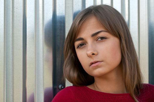 Portrait of a beautiful young girl in a red dress against the iron wall