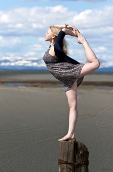 girl gymnast standing on one leg on a wooden post against the backdrop of mountains and the sky