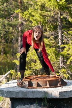 Woman tries to lift rusty manhole cover on a forest