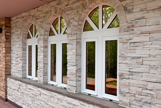 Three windows in the stone wall with a reflection of the forest